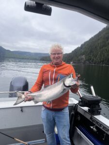 A man holding a big fish on a boat with mountains in the back